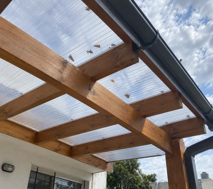 Pérgola de madera adosada con techo de policarbonato, vista desde el jardín