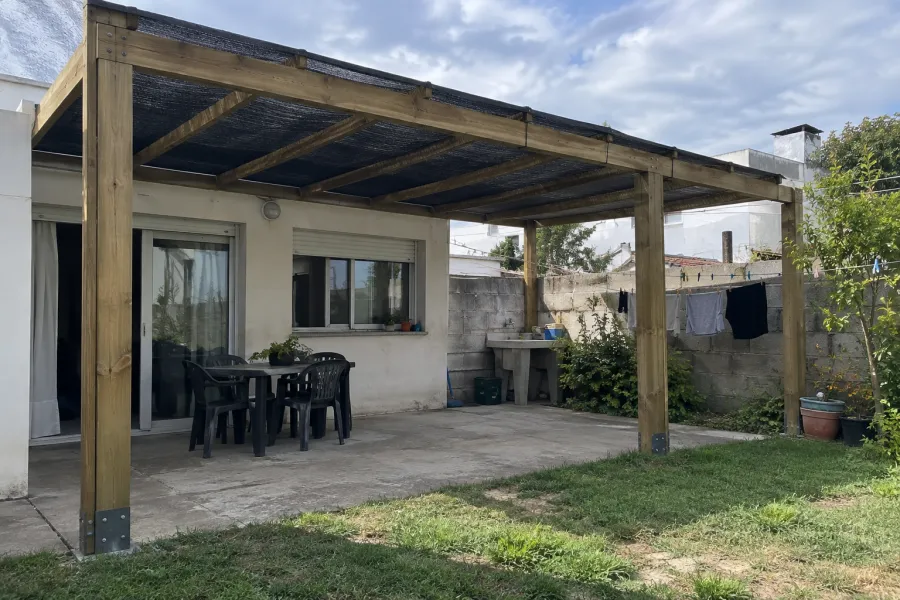 Pérgola de eucalipto con malla de media sombra tensada sobre los tirantes, en el fondo de una casa